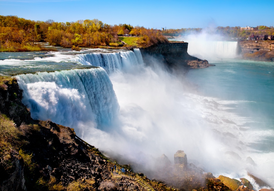 Fall colors on the American side of Niagara Falls in full flow with water mist rising.