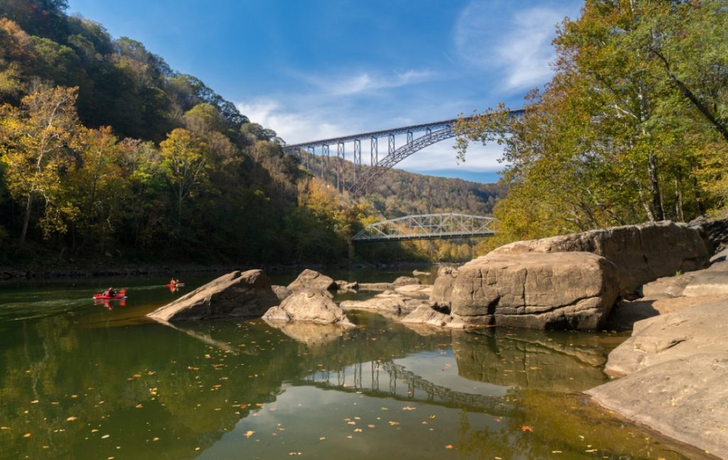 Kayakers float towards the rapids under the high arched New River Gorge bridge in West Virginia