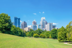 View of the Midtown Atlanta Georgia skyline from a green grassy park with a treeline in the foreground
