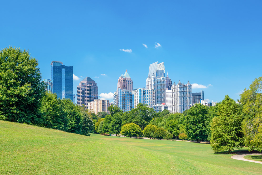 View of the Midtown Atlanta Georgia skyline from a green grassy park with a treeline in the foreground
