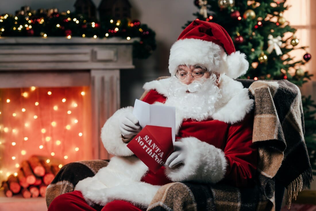 Santa sitting by the fire holding a stocking in grotto