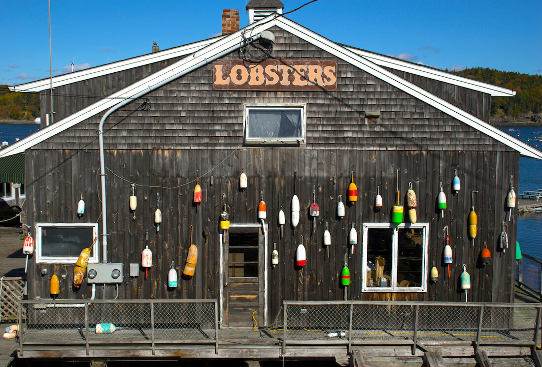 A coastal building says Lobsters and has colorful small buoys attached, seen near Bar Harbor Maine