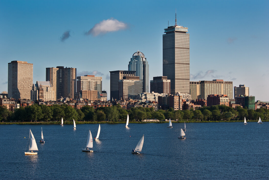 View of the Boston skyline from the Charles River Esplanade with multiple sailboats on the water in between