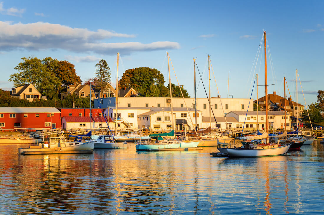 Golden light at sunset hits the buildings along Camden Harbor in Maine