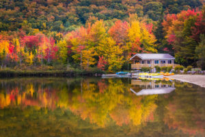 A boathouse on Echo Lake Beach in Franconia, New Hampshire, backed by trees in autumn colors reflecting on the lake