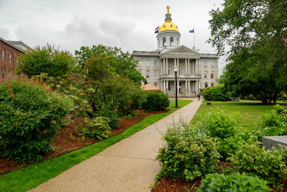 Tree lined path leading to New Hampshire State Capitol with gold dome top in Concrod