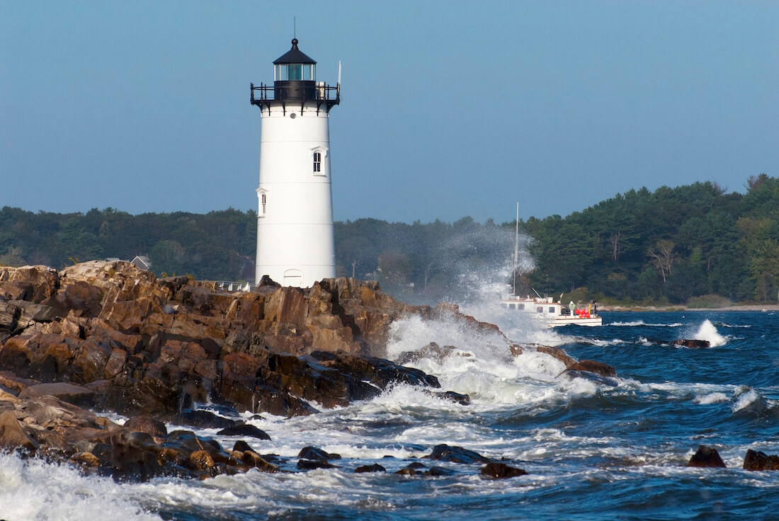 Fort Constitution Lighthouse or Portsmouth Lighthouse standing along the rocky shoreline with crashing winter waves and a boat navigating past the point