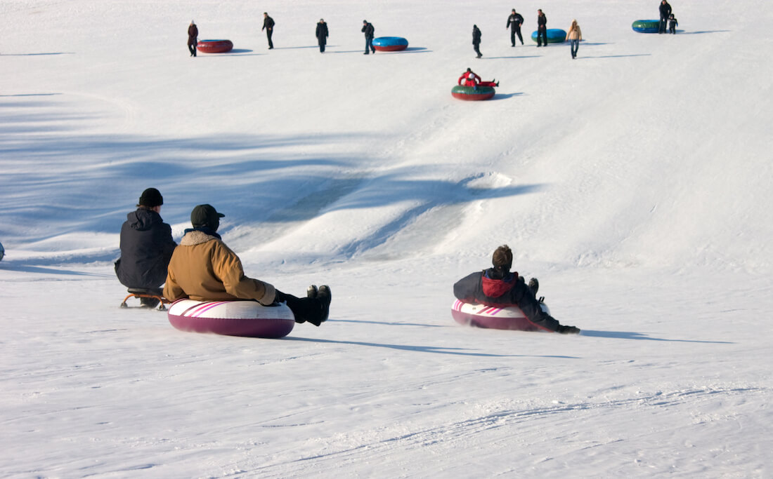 People sledding and tubing downhill in snow in winter