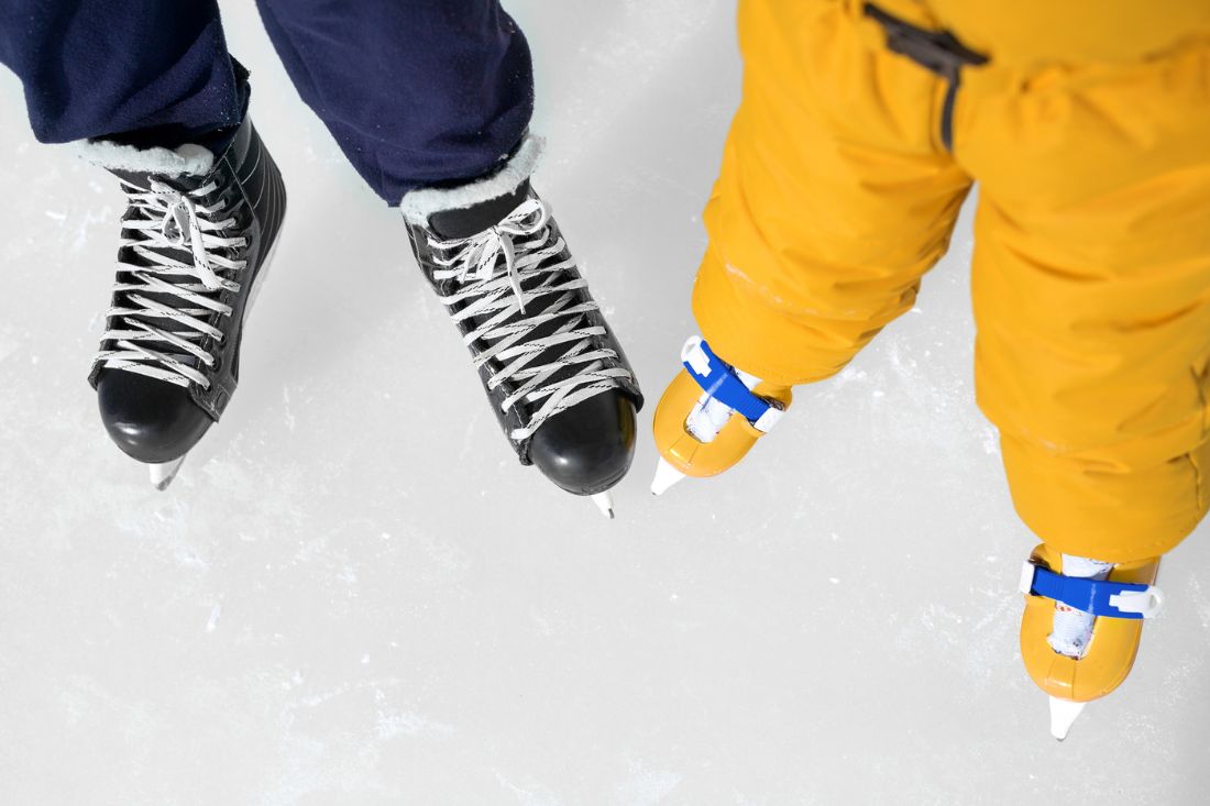 Close up photo of a man's black and a child's yellow ice skate on ice.