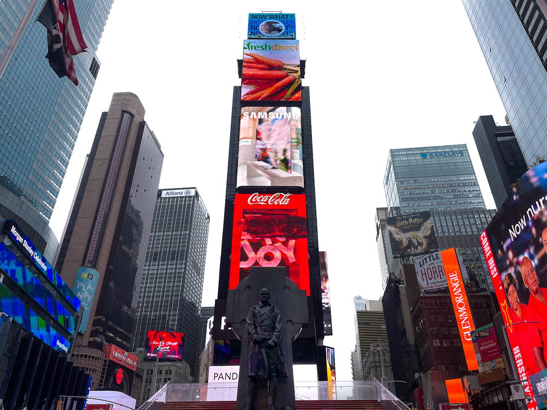 Statue and Red Steps surrounded by buildings with LED screen in Times Square, NYC.