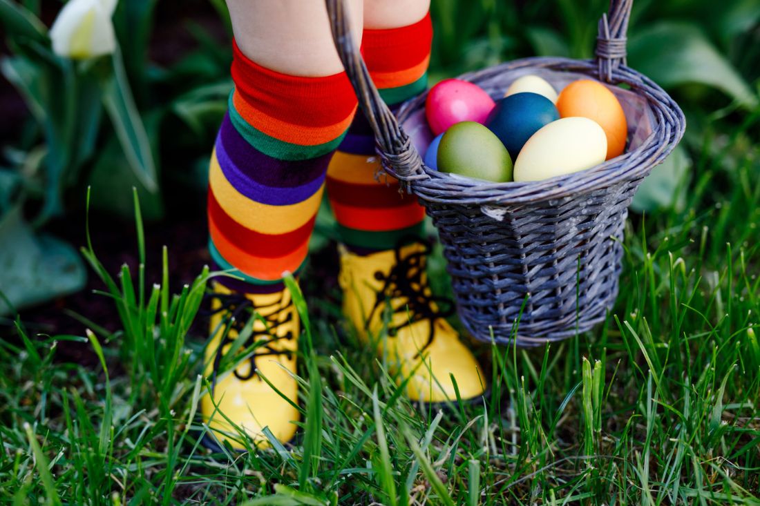Child in colorful rainbow stocking holding basket full of Easter eggs.