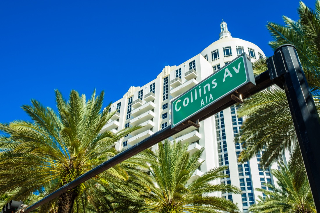 Collins Av sign against white building and palm trees in Miami Beach Florida. 