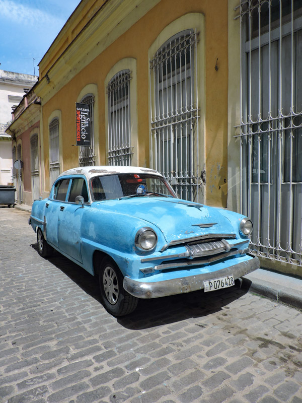 Blue vintage car against yellow building in Havana Cuba