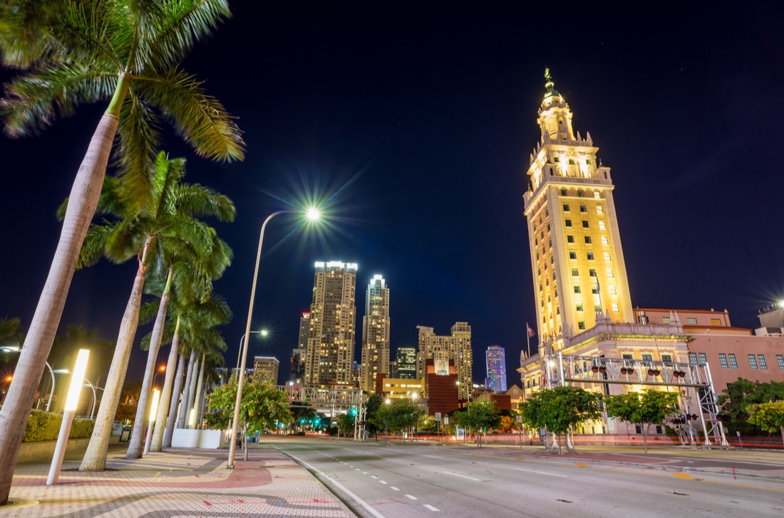 Miami Freedom Tower lit up at night on road with palm trees