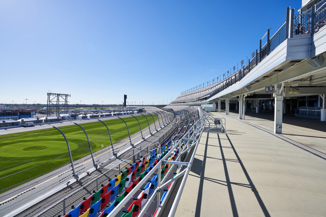 A platform in the seating area of the grandstands at Daytona International Speedway. It is a sunny day with blue sky, the grass is green, and seating is empty.
