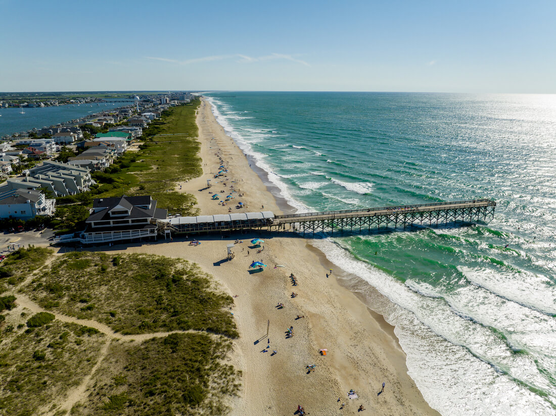 Aerial view of Johnnie Mercers fishing pier and beachfront houses on Wrightsville Beach in the Outer Banks of North Carolina