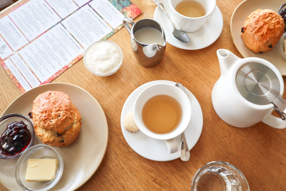 Flatlay of cup of tea, tea pot and scone on table