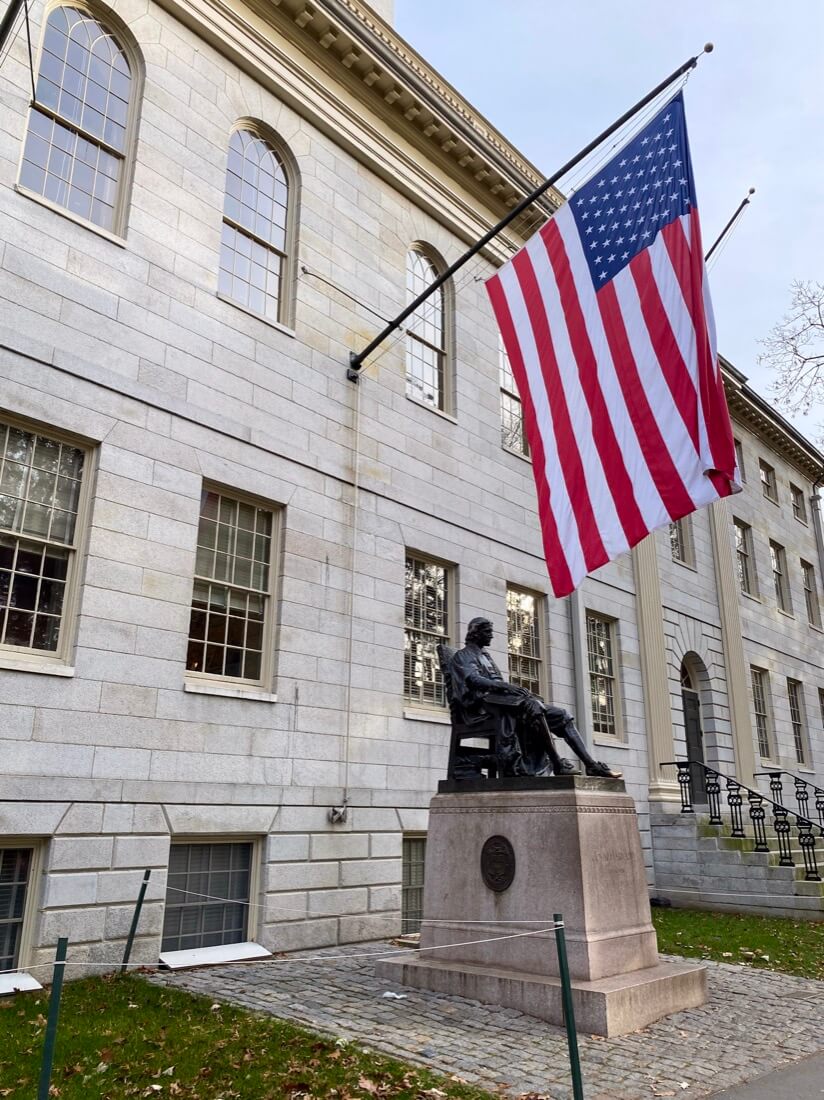 US Flag and Statue of John Harvard on Harvard University campus in Cambridge Massachusetts
